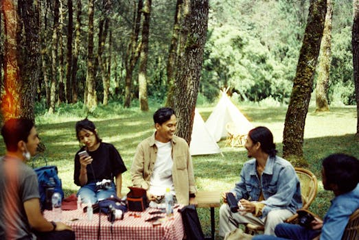 A group of friends enjoying a picnic in a forest with tents and nature around.